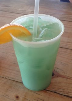 a green drink with an orange slice on the rim and a straw sticking out of it