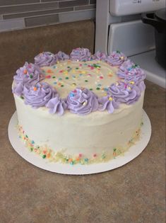 a white cake with purple frosting and sprinkles on the top sitting on a counter