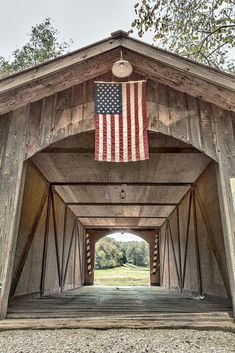 an american flag hanging from the side of a wooden covered structure with gravel and trees in the background