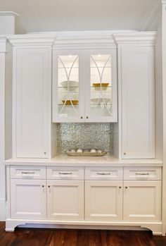 a white cabinet with two glass doors and cupboards on the front, in a room with hardwood floors