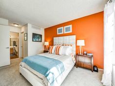 a bedroom with an orange accent wall, white bedding and two lamps on either side of the bed