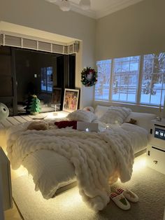 a bed that is made up with blankets and lights on the headboard, in front of two windows