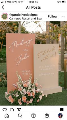 two pink and white wedding signs sitting on top of a lush green field next to flowers