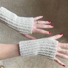 two hands wearing white knitted gloves with red nail polish and gold rings on them