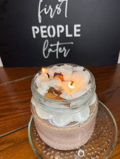 a glass jar filled with candles on top of a wooden table next to a sign