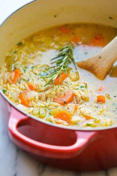 a red pot filled with chicken noodle soup next to a wooden spoon on a white counter