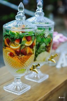 two glass containers filled with different types of fruit and veggies on top of a wooden table