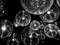 many shiny disco balls hanging from the ceiling in black and white with lights on them