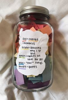 a jar filled with lots of different colored paper notes on top of a white sheet