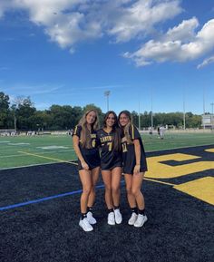 three girls in black and gold uniforms standing on a football field