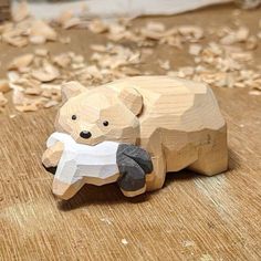 a wooden bear holding a piece of paper on top of a wood floor covered in leaves