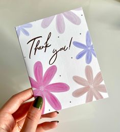 a hand holding up a thank card with pink and purple flowers on it that says, thank you