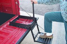 a man is sitting on the back of a red truck and pulling something with his feet