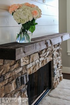 a vase filled with white and pink flowers on top of a mantle in front of a fireplace