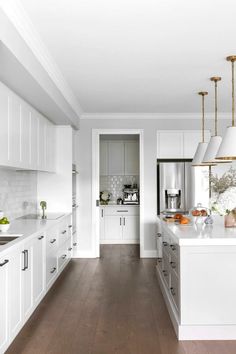 a large kitchen with white cabinets and wood flooring is pictured in this image, there are two pendant lights hanging over the island