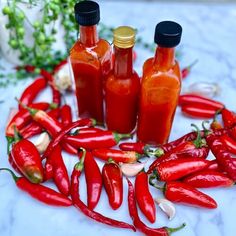 several bottles of hot sauce sitting on top of a table next to garlic and peppers