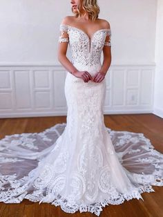 a woman in a white wedding dress standing on a wooden floor with her arms behind her back