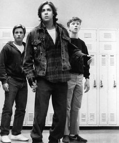 three young men standing in front of lockers, one wearing a jacket and jeans