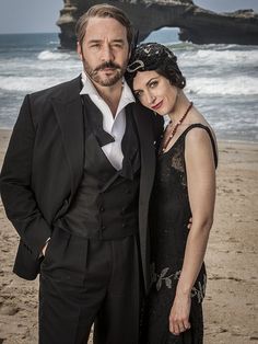 a man in a tuxedo standing next to a woman on the beach