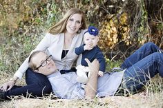 a man, woman and child laying on the ground in front of some brush with trees