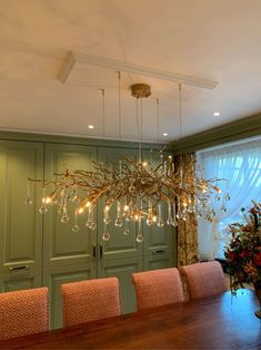 a chandelier hanging over a wooden table in a room with green walls and curtains