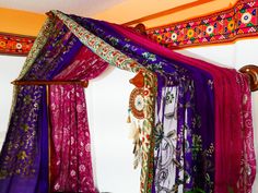 a canopy bed covered in colorful scarves and blankets