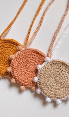 three crocheted round purses with tassels hanging from each side on a white surface