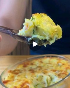 a person holding a spoon full of food over a casserole in a glass dish