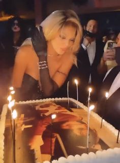 a woman blowing out candles on a cake with other people in the background looking at it