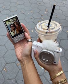 a person holding up a cell phone and taking a picture with a camera next to a cup of coffee