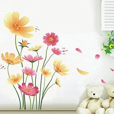 a teddy bear sitting next to a wall with flowers on it