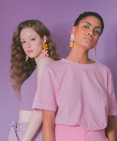 two models in pastel clothing with large earrings on their ears, one wearing a pink top