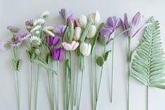 several crocheted flowers and leaves are arranged on a white surface with green stems