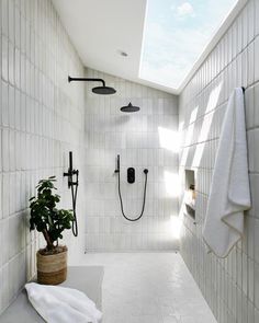 a white tiled bathroom with two shower heads and a potted plant in the corner