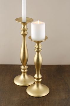 two brass candlesticks on a wooden table with a white candle in the middle