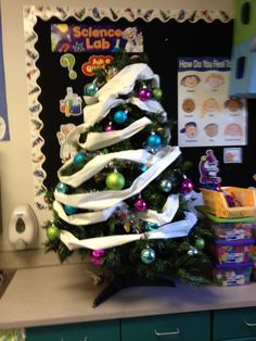 a christmas tree decorated with white ribbon and ornaments in the corner of a classroom room