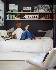 a person sitting on a bed reading a book in a room with bookshelves