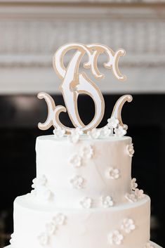 a wedding cake with white frosting and a wooden monogrammed initials on top