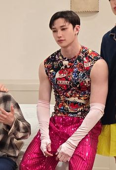 two men sitting next to each other in front of a white wall and one wearing pink gloves