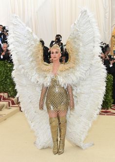 lady in gold and white outfit with huge angel wings on the red carpet at an event