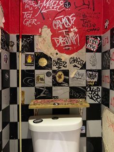 a white toilet sitting in a bathroom next to a checkered wall covered in graffiti