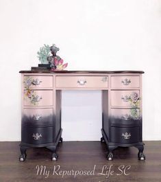 an antique desk with flowers painted on the top and black legs, is shown in front of a white wall