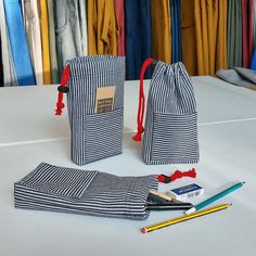 two bags and pencils on a table with clothes hanging in the backgroung