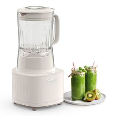 a blender sitting next to two glasses filled with green smoothies