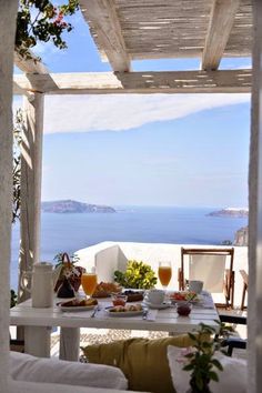 an outdoor table with food and drinks on it near the ocean in front of a white building