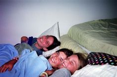 two women and a man are laying in bed together, one is smiling at the camera