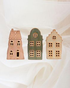 three small wooden houses sitting next to each other on a white cloth covered bed sheet