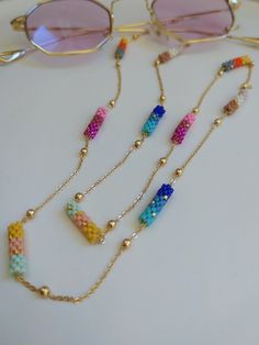 three necklaces with beads and sunglasses on top of a white table next to some glasses