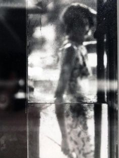 a black and white photo of a woman standing in front of a window