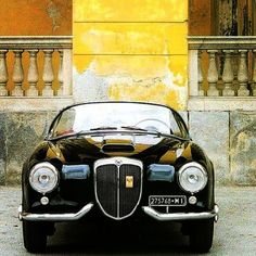 an old black car parked in front of a yellow building